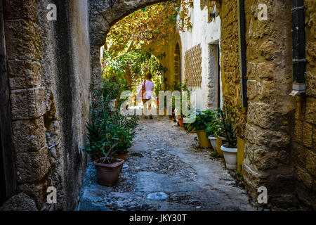 Seule femelle traveler walking cours des deux chats errants dans une ruelle de la ville méditerranéenne de Rhodes, Grèce Banque D'Images