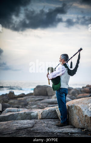 L'homme jouant sur la cornemuse sur la côte de l'océan dans l'Espagne, l'Europe, Muxia, Camino de Santiago. Banque D'Images