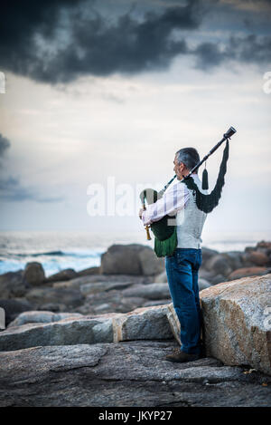 L'homme jouant sur la cornemuse sur la côte de l'océan dans l'Espagne, l'Europe, Muxia, Camino de Santiago. Banque D'Images