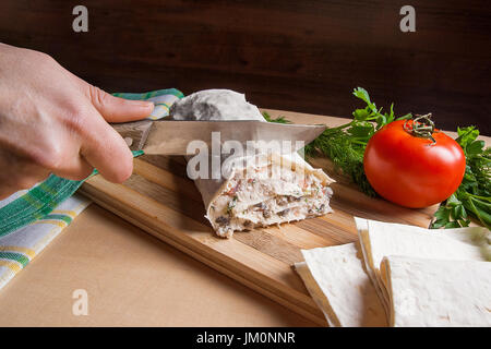 Woman's hand avec couteau dans ce mince coupe pain pita arménienne ou enveloppé lavash tomate, fromage cottage ou fromage, viande de poulet, tomates et fines herbes - Banque D'Images