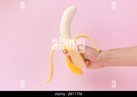 Tenir la main de bananes épluchées mâle isolé sur fond rose. Banque D'Images