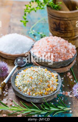 Différents types de sel naturel dans des bols en pierre sur la surface en bois. Sel de mer blanche, rose sel de l'Himalaya, sel épicé au romarin Banque D'Images