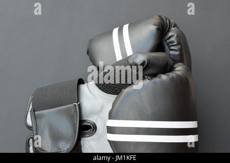 Paire de gants de boxe noir avec bandes blanches sur fond sombre. Banque D'Images
