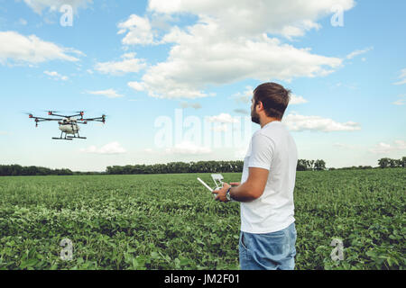 Jeune homme d'exploitation drone octocopter vol au champ vert. Banque D'Images