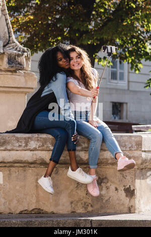 Deux jeunes abd belles femmes faisant près du monument selfies dans le centre-ville. Les femmes portant des vêtements décontractés. Une femme est noire. Banque D'Images