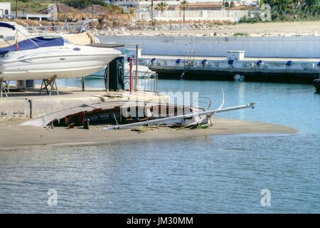 Bateau à voile coulé pris dans le sable après une tempête à l'entrée du port de Cabopino. Banque D'Images