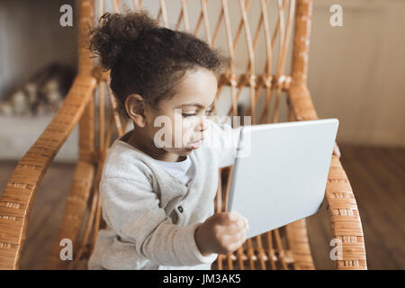 Adorable petit african american girl using digital tablet et assis sur un fauteuil à bascule à la maison Banque D'Images