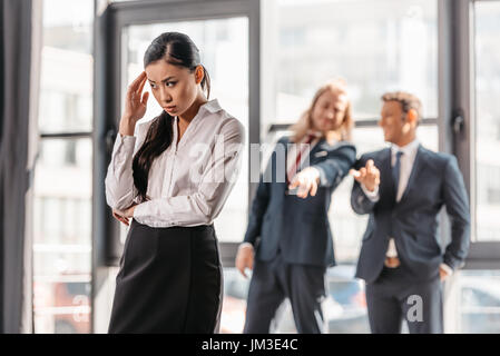 Frustrés asian businesswoman standing in office, hommes d'affaires derrière les gestes et de rire Banque D'Images