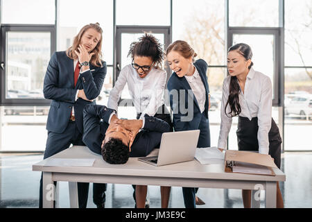 Trois jeunes femmes en colère punir businessman lying on table, réunion de l'équipe business concept Banque D'Images