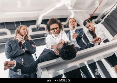 Trois jeunes femmes en colère punir businessman lying on table, réunion de l'équipe business concept Banque D'Images