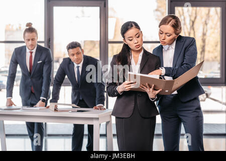 Deux jeunes femmes travaillant ensemble avec dossier lorsque debout derrière les hommes d'affaires, concept de travail d'équipe Banque D'Images