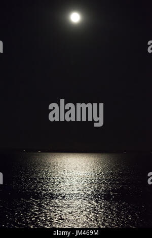 Pleine lune brillant haut dans le ciel nocturne avec reflet de lune sur l'eau dans Provincetown MA Banque D'Images