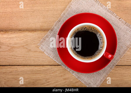 Grand gobelet plein de café instantané noir avec rouge soucoupe en porcelaine sur mousse sur table en bois avec nappe textile serviette de table, Close up, augmentation de la vue d'en haut, Banque D'Images