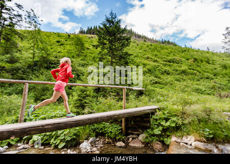 Jeune femme tournant dans les montagnes de l'été journée ensoleillée. Femme Trail Runner crossing bridge sur une rivière de montagne. Concept Sport et fitness en plein air dans n Banque D'Images