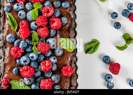 Maison d'été de boulangerie. Tarte au chocolat Gâteau au chocolat avec crème fraîche, framboise, myrtille baies brutes avec les feuilles de menthe, le sucre en poudre. White Banque D'Images