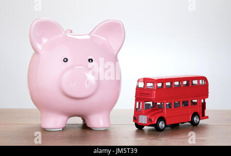 Pink piggy bank aux côtés d'un modèle à l'échelle d'un jouet London bus à impériale rouge dans une image conceptuelle des coûts des transports, vacances et tourisme Banque D'Images