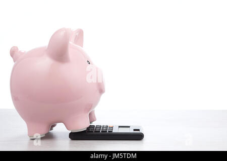 Peu de gras pink piggy bank permanent sur une calculatrice dans une vue de côté avec copie espace sur blanc dans une image conceptuelle des finances publiques, la richesse, les coûts, Banque D'Images