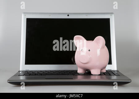 Pink piggy bank sitting on open laptop Banque D'Images
