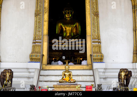 Statue de Bouddha et les gens priant vu à travers l'entrée de la grande salle de prière au Wat Suthat Thepwararam, un temple bouddhiste à Bangkok, Thaïlande. Banque D'Images