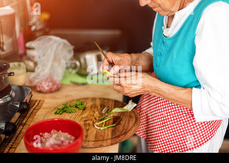 Senior woman mains hacher les légumes sur une planche en bois dans la cuisine. Banque D'Images