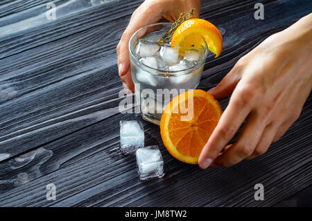 Préparation d'une boisson rafraîchissante avec de la glace et d'agrumes sur une table en bois sombre. Les mains de barman au travail de près. Conception du verre avant Banque D'Images