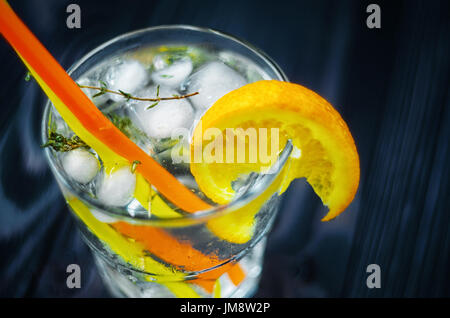 Gin Tonic avec ice, décoré avec une tranche d'orange et le romarin. Banque D'Images