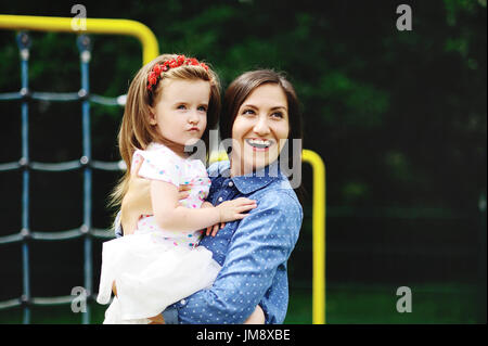 Jeune mère joue dans l'aire de jeux avec la petite fille. La femme tient le bébé sur les mains. Elle appuie doucement à elle-même la fille. Banque D'Images