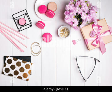 Les fleurs roses, macarons, bougie, verres et autres accessoires féminin petit mignon sur la table en bois blanc Banque D'Images