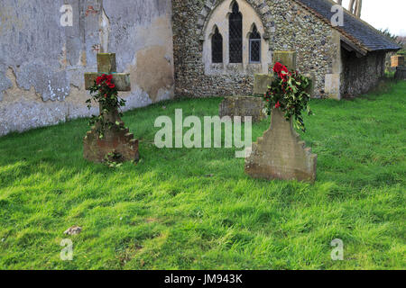 Les pierres tombales de la famille à l'église cimetière décoré de houx pour Noël, Shottisham, Suffolk, Angleterre, RU Banque D'Images