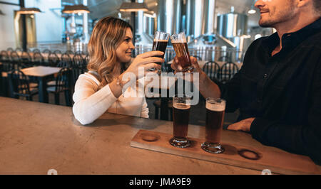 Couple au bar avec différentes variétés de bières artisanales. Ils sont à Brewery et toasting beer glasses. Banque D'Images