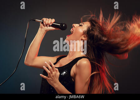 Une jeune femme chanteuse avec de longs cheveux ébouriffés tenant un micro et chanter avec une bouche grande ouverte. Banque D'Images