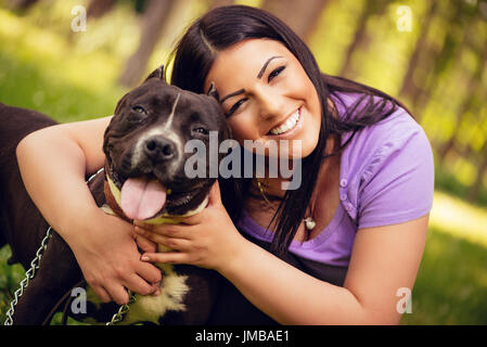 Portrait d'une belle jeune femme hugging her cute stafford terrier dans le parc et d'apprécier. Regardant cemera. Banque D'Images