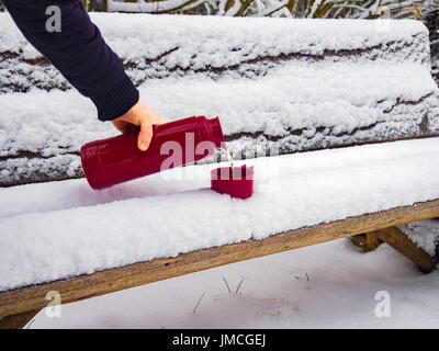 Verser le thé chaud de l'homme en thermos tasse en plastique de l'article sur un banc recouvert de neige Banque D'Images