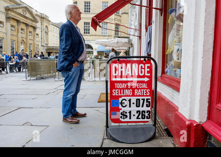 Un homme debout à côté d'une carte d'affichage du taux de change est représenté à la recherche dans un des bureaux de change situés dans une boutique touristique à Bath, Angleterre Banque D'Images