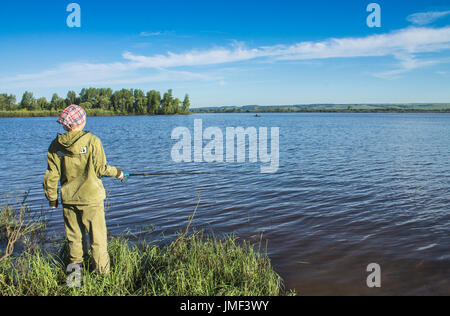 Une jeune femme en vert vêtements est debout sur la rive du fleuve et la pêche avec une canne à pêche. Banque D'Images