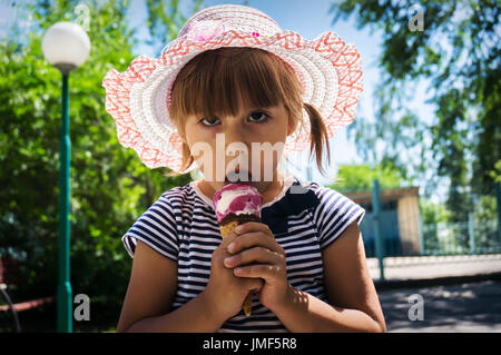 La douce enfant lèche la crème glacée dans un cornet gaufré dans le jardin Banque D'Images