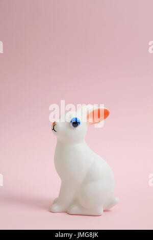 Un mignon petit lapin blanc en plastique portant l'œil adhésif poupée sur un fond rose. Couleur minimum still life photography Banque D'Images