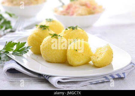 Boulettes de pommes de terre fraîchement préparé servi sur un plateau blanc, choucroute avec bacon dans l'arrière-plan Banque D'Images