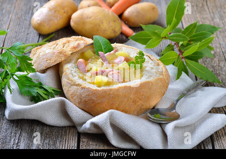 Soupe de pommes de terre fraîchement faite avec bacon et saucisses de Vienne servi dans les roues une miche de pain Banque D'Images