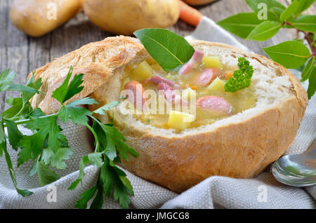 Soupe de pommes de terre fraîchement faite avec bacon et saucisses de Vienne servi dans les roues une miche de pain Banque D'Images