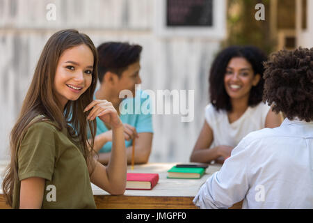 Image jeunes groupe multiethnique d'amis étudiants à parler les uns avec les autres à l'extérieur. Jolie dame à la caméra. Banque D'Images