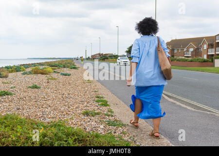 Femme marchant le long d'une route par un front de plage sur un jour de vent. Banque D'Images