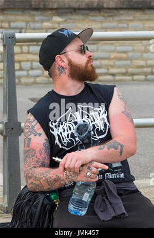 Tattooed man sitting on wall de promenade à Lyme Regis, dans le Dorset en Juillet Banque D'Images