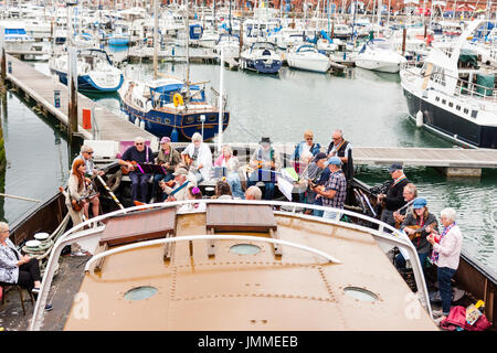 Concert par l'accord groupe, The Sunshine Ukes sur le dos d'un remorqueur, le Cervia, ancrés dans le port au cours de la fête de Ramsgate. Principalement des aînés, hommes et femmes, assis sur le pont arrière du bateau. Banque D'Images