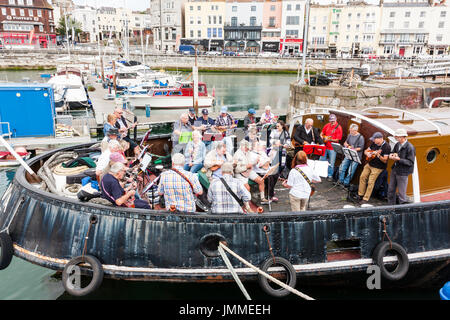 Concert par l'accord groupe, The Sunshine Ukes sur le dos d'un remorqueur, le Cervia, ancrés dans le port au cours de la fête de Ramsgate. Principalement des aînés, hommes et femmes, assis sur le pont arrière du bateau. Banque D'Images