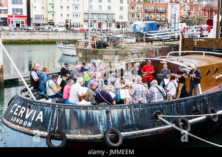 Concert par l'accord groupe, The Sunshine Ukes sur le dos d'un remorqueur, le Cervia, ancrés dans le port au cours de la fête de Ramsgate. Principalement des aînés, hommes et femmes, assis sur le pont arrière du bateau. Banque D'Images