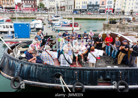 Concert par l'accord groupe, The Sunshine Ukes sur le dos d'un remorqueur, le Cervia, ancrés dans le port au cours de la fête de Ramsgate. Principalement des aînés, hommes et femmes, assis sur le pont arrière du bateau. Banque D'Images