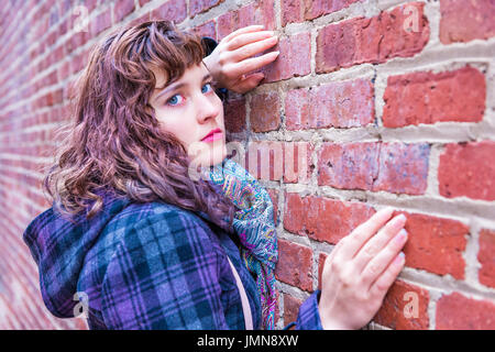 Young woman leaning against brick wall en enduire au cours de l'hiver Banque D'Images