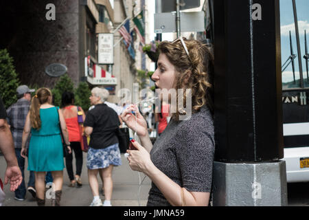 Avec une jeune femme, les cheveux bouclés, parler au téléphone à l'aide de casque / écouteurs, le holding microphone pièce dans sa main, tout en se tenant sur la rue Banque D'Images