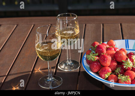 Fraises fraîches dans un bol et deux verres de vin sparklning sur une table en bois Banque D'Images
